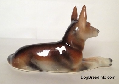 The right side of a brown and white with black lying German Shepherd figurine. The ears of the figurine are alert.