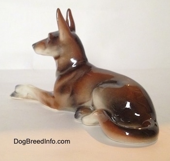 The back left side of a figurine of a brown and white with black German Shepherd lying figurine. The figuirine has its long white legs sticking out and it has black tipped nails.