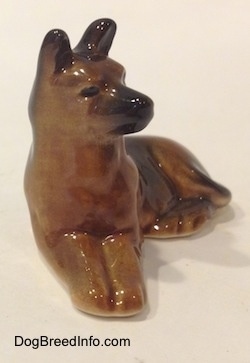A brown with black figurine of a Shepherd in a lying pose. The figurine has curves instead of points.