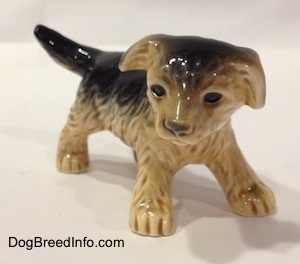 The front right side of a figurine of a black with tan German Shepherd puppy. The figurine has black circles for eyes and the eyes have a gloss to them.