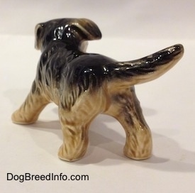The back left side of a black with tan German Shepherd puppy figurine. The figurine has a tail that is the length of its body.