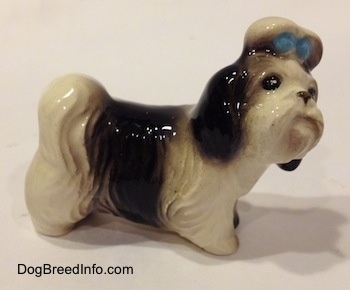 The right side of a white with black Shih Tzu figurine with a blur bow in its hair. The figurine is looking up and to the right.