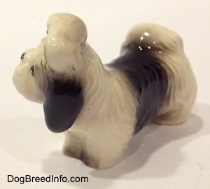 The front left side of a figurine of a white with black figurine of a Shih Tzu with a blue bow in its hair. The figurine has a large black spot on its back.