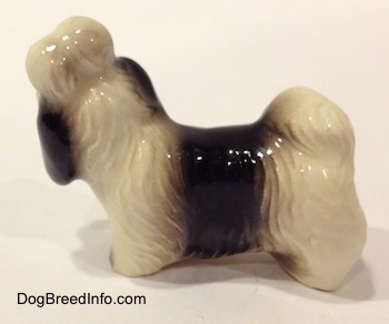 The left side of a white with black Shih Tzu with a blue bow in its hair figurine. The figurine has short legs.