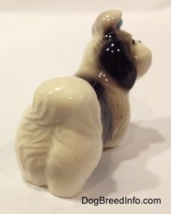 The back right side of a white with black Shih Tzu figurine with a blue bow in its hair. The figurine is glossy.