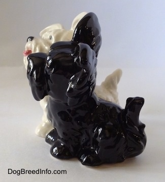 The left side of a figurine sitting of two Skye Terriers. The figurines have short tails that are in the air.