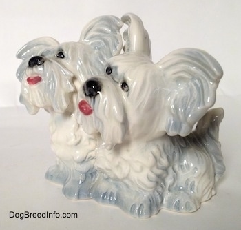 The front left side of a silver platinum figurine of a Siamese twin Skye Terrier sitting. The figurines have short legs.