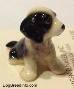 The front right side of a figurine of a black with white English Sprigner Spaniel puppy in a sitting pose. The ears of the figurine are hard to differentiate from its head.