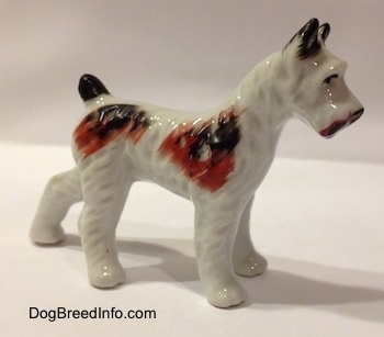The front right side of a white with brown and black porcelain figurine of a Standard Schnauzer. The figurine has short ears.
