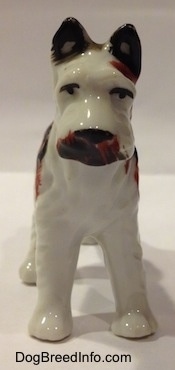 A porcelain white with brown and black Standard Schnauzer figurine. The figurine has black circles for eyes and brown around its mouth.