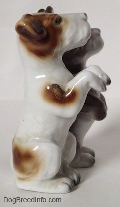 THe right side of two figurines of Jack Russell Terriers that are in a begging pose. The most forward figurine is white with brown.