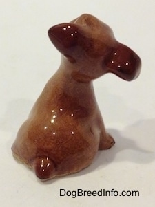 The back of a brown figurine of a Terrier puppy figurine. The figurine has a short tail.