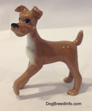 A tan with white figurine of a dog. The figurine has long legs.