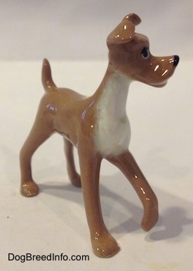 The front right side of a figurine of a tan with white dog. The figurine looks like 'Tramp' from 
   Disneys The Lady and The Trump'.