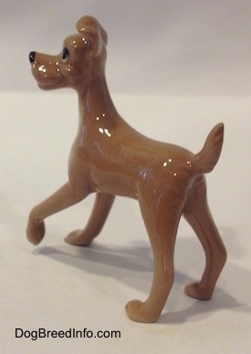 The back left side of a figurine of a dog that is tan with white. The figurine is glossy.