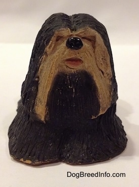 A black with tan figurine of a standing Tibetan Terrier. Its mouth is painted open.