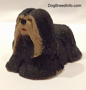 The front left side of a figurine of a black with tan Tibetan Terrier standing. The figurine has a black circle for a nose.