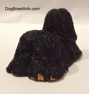 The back right side of a black with tan figurine of a Tibetan Terrier. The figurines tail is hard to differentiate from its body.