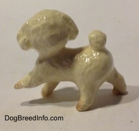 The left side of a white with brown figurine of a walking Toy Poodle. The figurine has short legs.