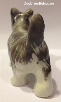 The back of a porcelain grey and white Miniature Schnauzer figurine. The figurine has a long tail that is arched in the air.