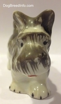 A porcelain figurine of a grey and white Miniature Schnauzer. The figurine has black circles for eyes