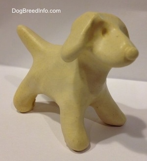 The front right side of a ceramic white dog that is unpainted.