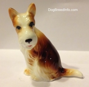 The left side of a brown and white bone china Wire Fox Terrier figurine. The figurine has black circles for eyes.