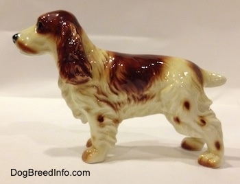 The left side of a red and white Welsh Springer Spaniel figurine. The figurine has spots up and down its legs.