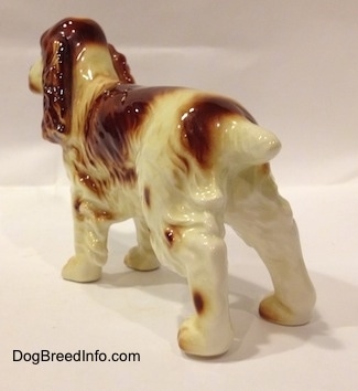 The back left side of a figurine of an orange and white standing Welsh Springer Spaniel. The figurine has a cropped tail.