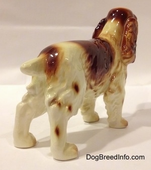 The back right side of a red and white standing Welsh Springer Spaniel figurine. The figurine has long legs.