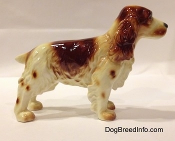 The right side of a standing red/orange and white figurine of a Welsh Springer Spaniel. The figurine has a large red/orange spot on its back.