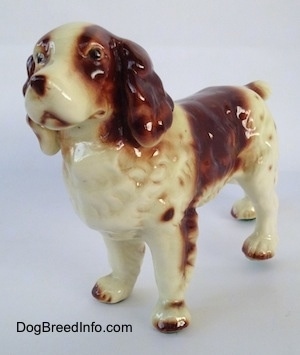 The front left side of a brown and white figurine of a Welsh Springer Spaniel. The figurine has black circles for eyes.