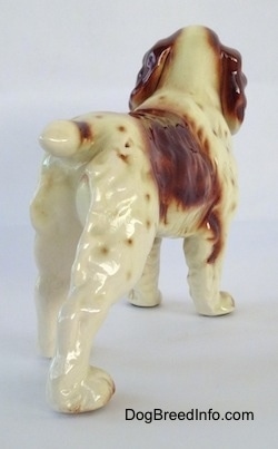The back right side of a figurine of a brown and white Welsh Springer Spaniel. The figurine has a short tail with a brown spot on it.