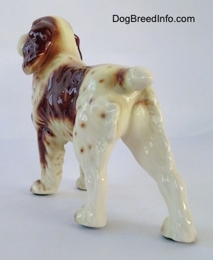 The back left side of a white and brown Welsh Springer Spaniel figurine. The figurine has long legs.