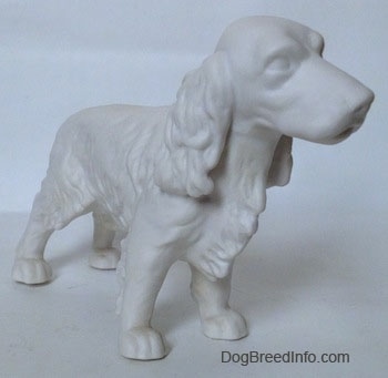 The front right side of an unpainted white bisque Welsh Springer Spaniel standing figurine. The figurines mouth is slightly open.