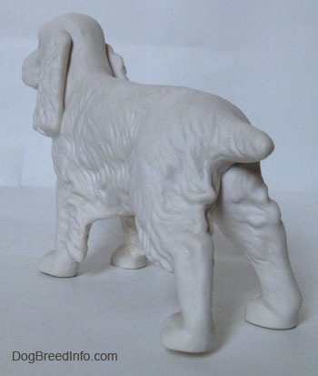 The back left side of a white bisque Welsh Springer Spaniel standing figurine. The figurine has long ears with fine hair details.