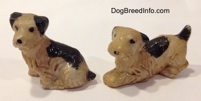 Two miniature  dingy white with black bone china Welsh Terrier puppies. One of the figurines is sitting and the other figurine is in a play bow pose.