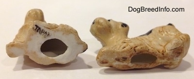 The underside of two miniature Welsh Terrier puppy figurines. They both have big holes on the underside and the left one has a black stamp that reads 'JAPAN'.