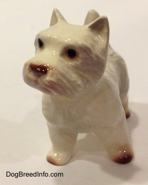 A white with tan figurine of a West Highland Terrier. The figurine has black circles for eyes.