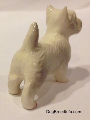 The back right side of a figurine of a white with tan West Highland Terrier. The figurine has a short tail in the air.