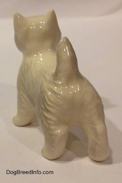 The back left side of a figurine of a white West Highland Terrier. The figurine has short legs.
