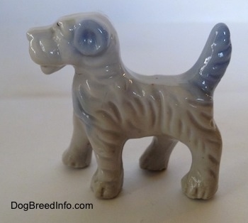 The right side of a porcelain figurine of a white with blue Wire Fox Terrier that has blue ears.