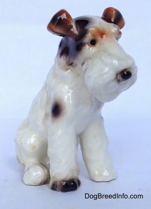 The front right side of a white with black and brown Wire Fox Terrier sitting figurine. The figurine has black circles for eyes.
