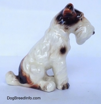 The right side of a white with black and brown Wire Fox Terrier figurine in a sitting pose. The figurine has fine hair details along its body.