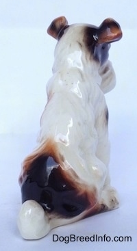 The back of a figurine of a white with black and brown Wire Fox Terrier sitting. The figurine has a short tail.