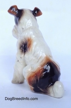 The back left side of a white with black and brown Wire Fox Terrier figurine in a sitting position. The figurine is glossy.