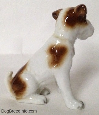 The right side of a white with brown Wire Fox Terrier figurine in a sitting position. The figurine has a brown patch above its leg.