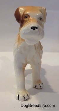 A standing figurine of a white and tan Wire Fox Terrier. The figurine has small black circles for eyes.