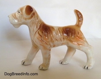 The left side of a white and tan Wire Fox Terrier figurine in a standing pose. The figurine has tan flopped over ears.