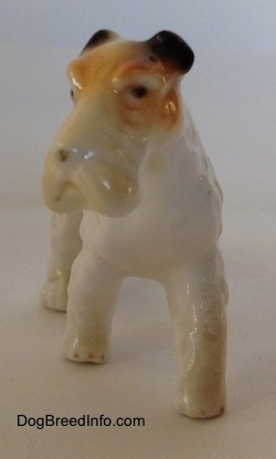 A figurine of a white with black and tan bone china Wire Fox Terrier. The figurine has small black circles for eyes.